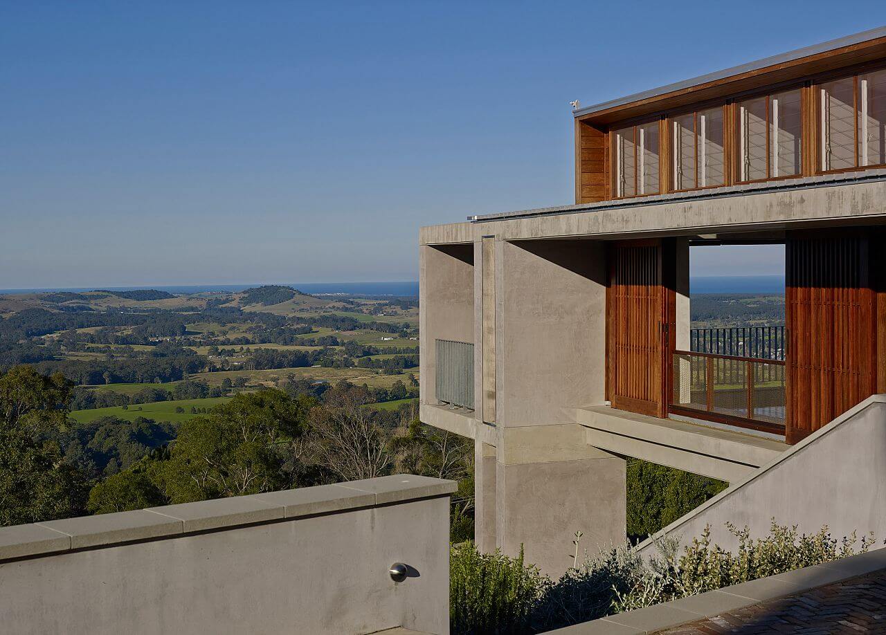 A concrete house featuring a wooden balcony that offers a scenic view of the surrounding valley