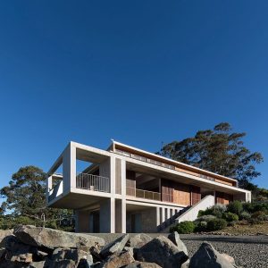 A sleek modern home situated on a hillside, framed by natural rocks and trees